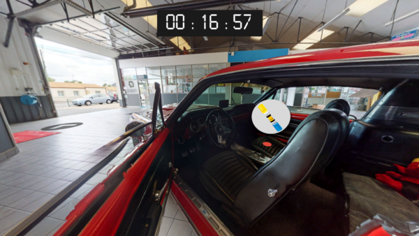 Ecran du serious game de sécurité routière de Pro In Sec. On voit un garage automobile en vue 360 degrés avec des flèches de direction et un objet à récupérer sur le siège d'une voiture.